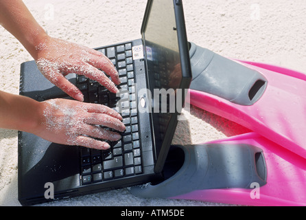 Sandy hands using laptop on beach during working holiday Stock Photo
