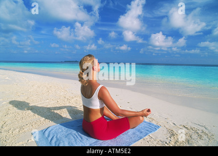 Woman on sandy shore in yoga position at dawn Stock Photo