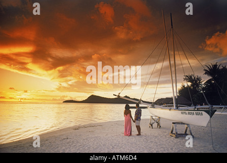 Couple standing on sandy Bora Bora shore holding hands under dramatic sunset sky Stock Photo