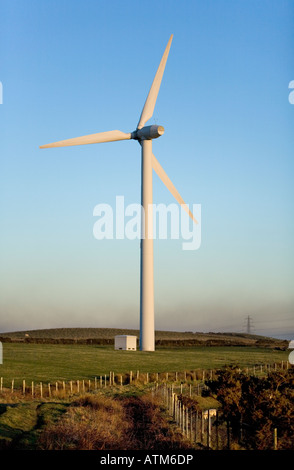 Single wind turbine on a hilltop against a late afternoon clear blue sky with sheep grazing on a hillside Stock Photo
