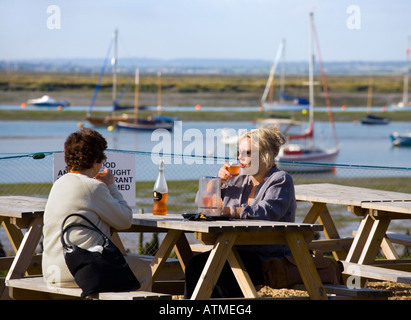 VISITORS TO WEST MERSEA HAVE A DRINK AT THE WATERFRONT WITH THE SEA AND MOORED BOATS IN THE BACKGROUND Stock Photo