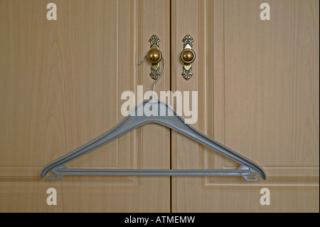 Grey plastic coat hanger hanging on handle of door of wardrope Stock Photo