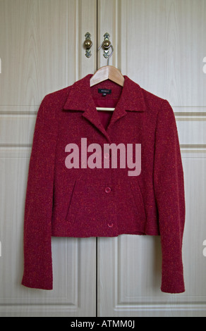 Red woman's jacket on wooden coat hanger hanging on handle of door of wardrope Stock Photo