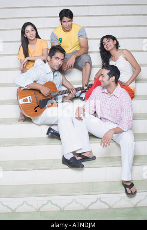 Young man playing a guitar with his friends sitting with him Stock Photo