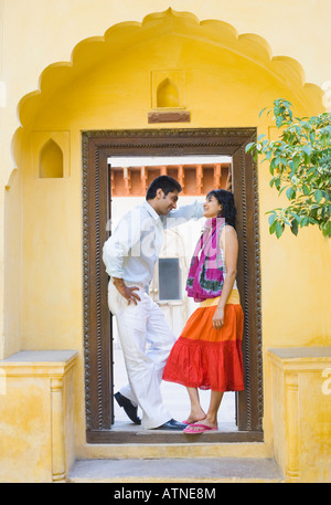 Side profile of a young couple standing at the entrance of a house and smiling Stock Photo