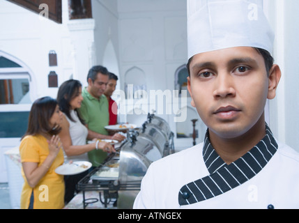 Portrait of a chef with two mid adult couples having food behind him Stock Photo