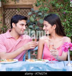 Young couple sitting at a dining table and holding champagne flutes Stock Photo