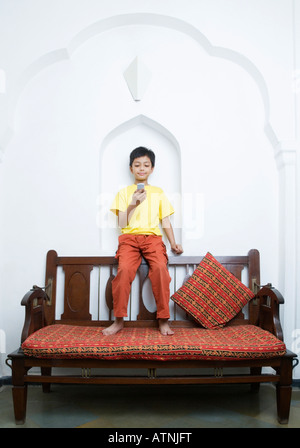 Boy sitting on top of a couch and using a mobile phone Stock Photo