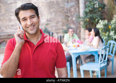 Portrait of a mid adult man talking on a mobile phone with his friends sitting at a dining table in the background Stock Photo