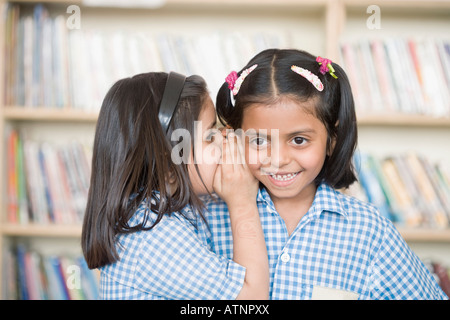 Side profile of a schoolgirl whispering into her friend's ear Stock Photo