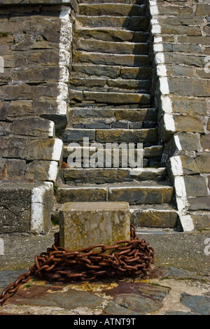 Old stone harbour quayside steps with stone mooring point and coiled round rusty chain Stock Photo