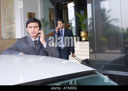 Businessman standing near a car and talking on a mobile phone Stock Photo
