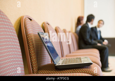 Laptop on a chair with three business executives sitting in the background Stock Photo