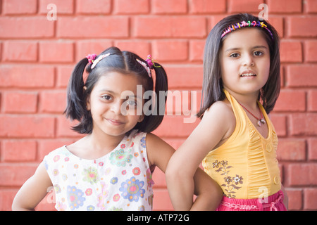 Portrait of two schoolgirls standing in front of a brick wall and smiling Stock Photo