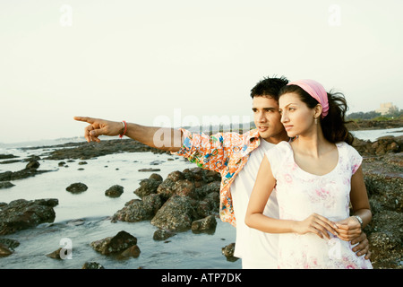 Young man pointing away to a young woman and standing on the beach Stock Photo