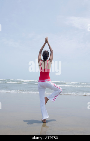 Rear view of a young woman standing in a tree pose on the beach Stock Photo