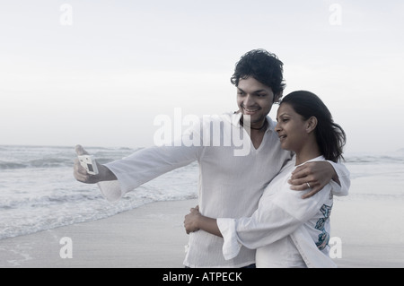 Young couple taking a picture of themselves with a digital camera on the beach Stock Photo