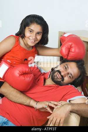 Portrait of a mid adult man reclining on a couch with his daughter wearing boxing gloves Stock Photo