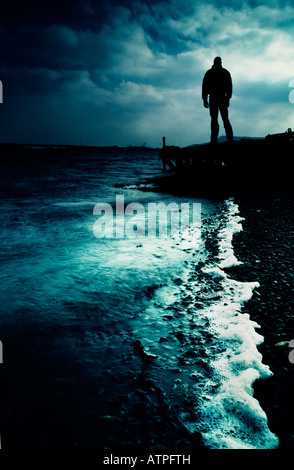 Dark figure standing on jetty looking out to sea Stock Photo