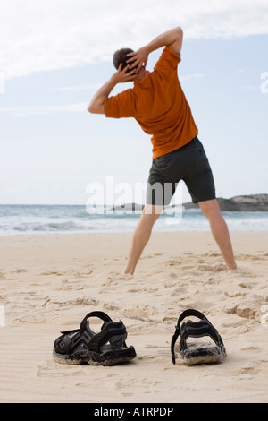 Man doing gymnastics on the beach Focus on his sandals in the foreground Stock Photo