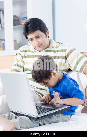 Boy using a laptop with his father sitting beside him Stock Photo