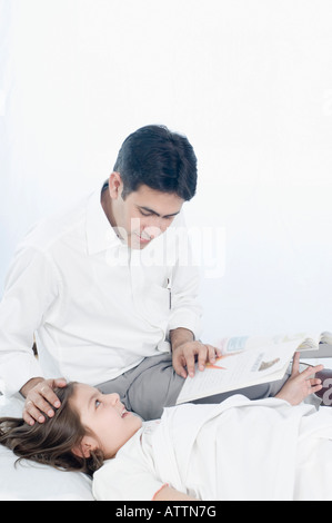 Mid adult man reading a book beside his daughter lying on the bed Stock Photo