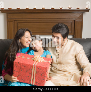 Close-up of a couple and their daughter sitting on a couch with a gift Stock Photo