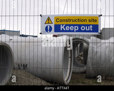 Construction site Keep out, sign hung on a fence with drainage pipes behind it. Stock Photo