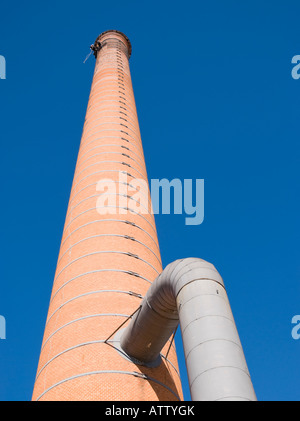 Cropped shot of an unrecognizable worker hanging from a high industrial brick chimney. Blue sky in the background. Stock Photo