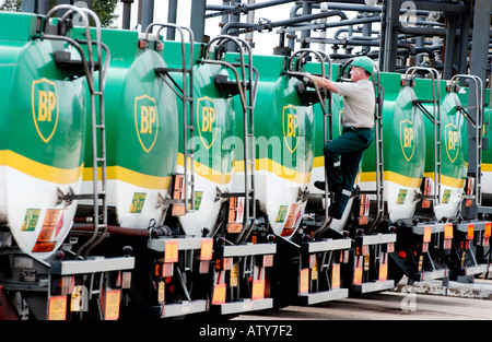 BP tankers lined up at an oil terminal with male worker in hard hat on inspection and access ladder at rear of tank. Stock Photo