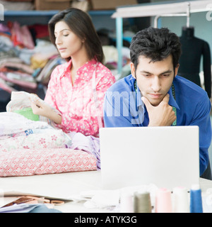Close-up of a male fashion designer using a laptop with a female fashion designer in the background Stock Photo