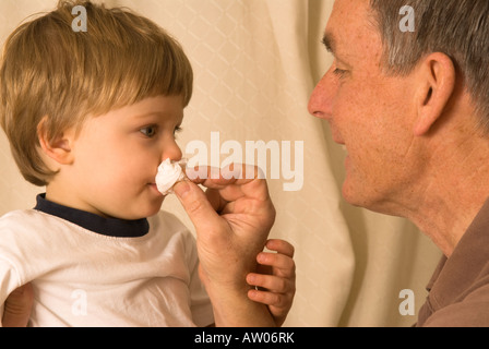 grandfather father wiping runny nose of son grandson two years old Stock Photo