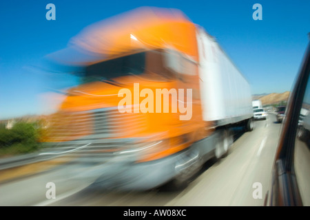 Bright orange semi truck speeding along freeway in Los Angeles,  California, USA with blurred motion time exposure, Stock Photo