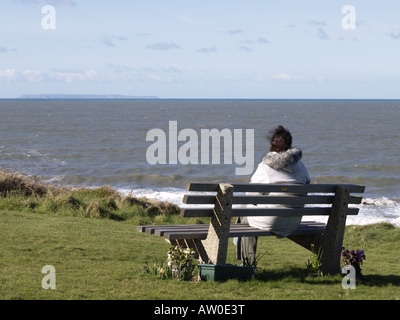 Woman sat on park bench looking out to sea at Lundy island Stock Photo