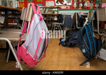 girls and boys schoolbag rucksacks hanging off the back of empty classroom chairs in primary school in belfast northern ireland Stock Photo