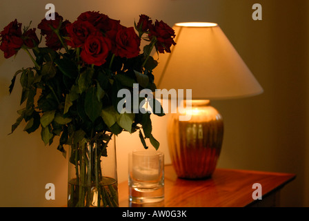 a table lamp and vase containing flowers in a hallway in subdued atmospheric lighting on a sideboard dresser Stock Photo