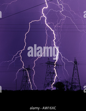 Lightning strikes against a dark purple sky near powerlines and power poles or electrical towers during a monsoon in Tucson Stock Photo