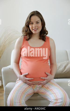 Pregnant woman sat on sofa Stock Photo