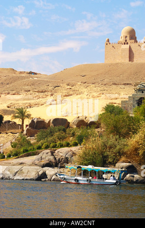 Motor cruise boat taking tourists past the Aga Khan's Mausoleum on the west bank of the River Nile at Aswan in Egypt Stock Photo