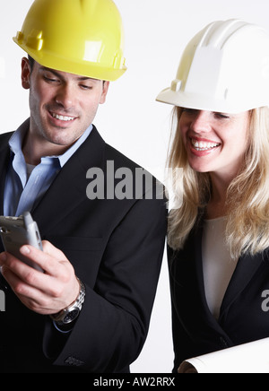 man and woman architects wearing hard hats looking at wireless computer device Stock Photo