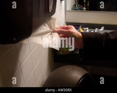 A caucasian woman extracts a paper towel after washing her hands in a public restroom. USA. Stock Photo