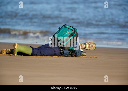 Man laying on beach with backpack and long lens photographing Seals at Donna Nook Lincolnshire Stock Photo