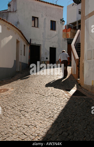 An elderly man walking in the cobbled street leading uphill toward Convento Nossa Senhora De Desterro monastery in Monchique town in Algarve Portugal Stock Photo