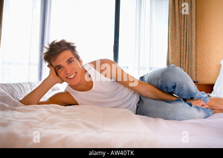 Young man smiles lays on bed. Stock Photo