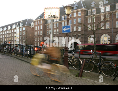 A cyclist rides past parked bicycles on a canal bridge in Amsterdam. Stock Photo