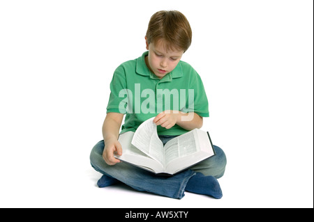 A young boy sat crossed legs turning the page of a reference book he is reading shot against a white background Stock Photo