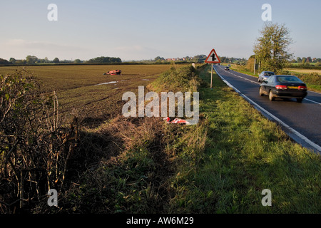 CRASHED CAR IN FIELD ALONGSIDE COUNTRY ROAD WITH TRAFFIC UK Stock Photo