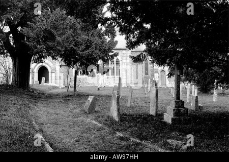 Little used side entrance pathway to St James Church in Christow on Dartmoor with gravestones and overhanging trees in mono Stock Photo