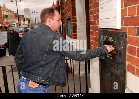 Man posting letter at his local post office High Street New Malden Surrey Stock Photo