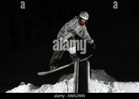 A young male snowboarder performs a freestyle stunt by sliding down or riding a railing Stock Photo